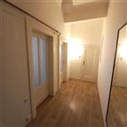 Široká chodba s dřevěnou podlahou, bílými dveřmi a výškou stropu, nabízí moderní design a světlé osvětlení.